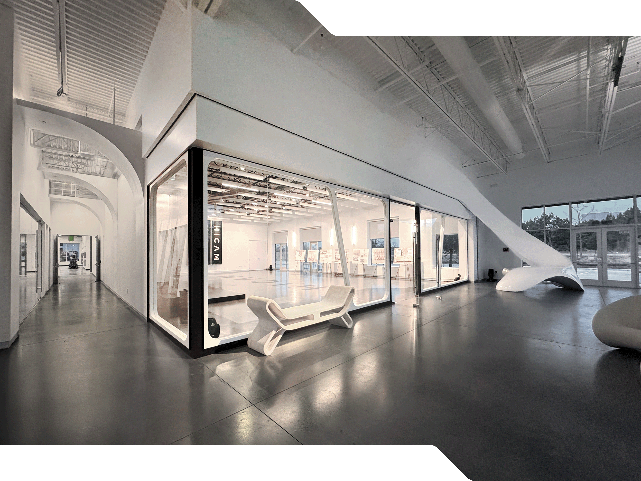 HICAM’s modern, spacious lobby with high ceilings, polished concrete floors, and sleek white architectural features. A large glass-walled event space room is centrally positioned, surrounded by sculptural furniture and natural light from large windows.